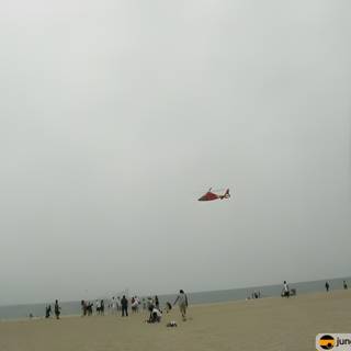 Red Helicopter Soaring over Beach-Goers