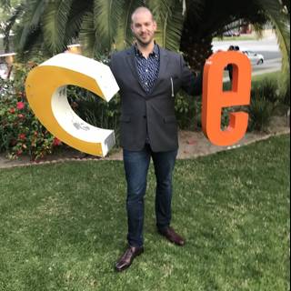 Man holding up a letter C on a grassy lawn