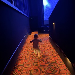 Child Running Through Illuminated Carpet Hallway in Dark Museum