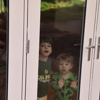 Two Children Peering Through Glass Door at Home