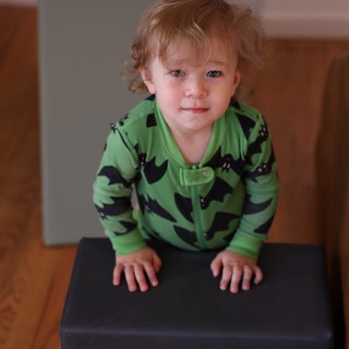 Toddler in Green Dinosaur Pajamas on Brown Couch