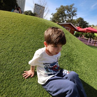 Boy Sliding Down Grassy Hill at Urban Park