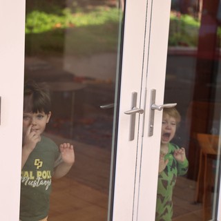 Two Young Boys Peering Through Glass Door
