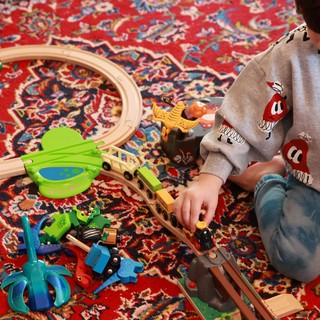 Child Playing with Wooden Train Set on Persian Rug