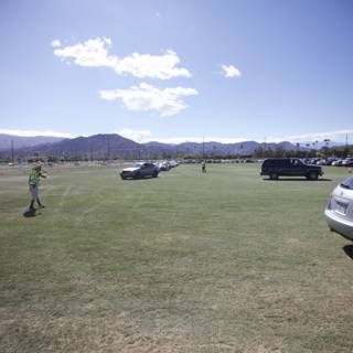 Kite-flying fun with a scenic view Caption: A person flying a kite in a grassy field with a mountain and a line of cars in the background during Coachella 2012.