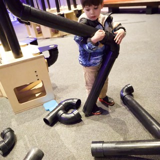 Child Exploring Interactive Pipe Construction Exhibit at Children's Museum