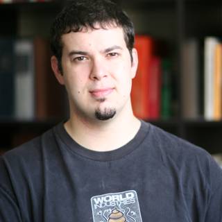 Man in black shirt poses in front of bookshelf