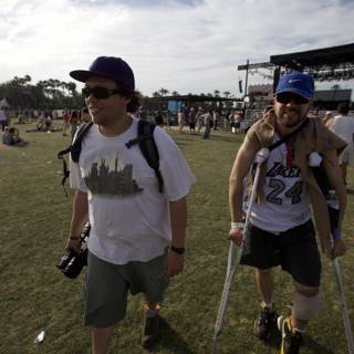 Overcoming Obstacles Caption: Two men in baseball hats walk on crutches through the lively Coachella crowd.