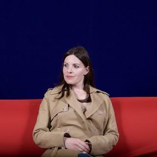 Woman in Trench Coat Seated on Red Sofa
