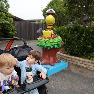 Two Young Boys in Stroller Near Cartoon Bird Statue