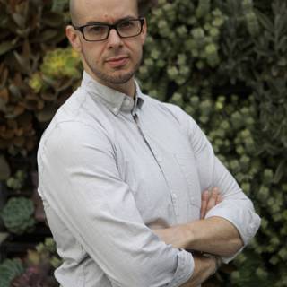 Portrait of a Man in Glasses Standing Amongst a Wall of Plants