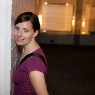 Woman Leans Against Wall With Playful Smile