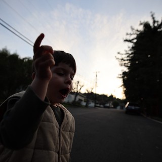 Young Boy Pointing at Dusk in Suburban Street