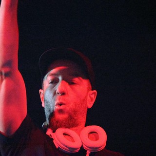 DJ Raises Hand Under Red Stage Lights at Wobbleland