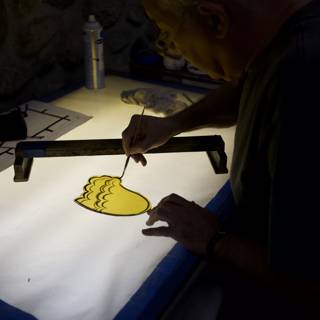 Working on Art: A Man Crafting with a Tool on a Yellow Surface