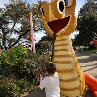 Child Encounters Whimsical Giant Snake Sculpture in Park