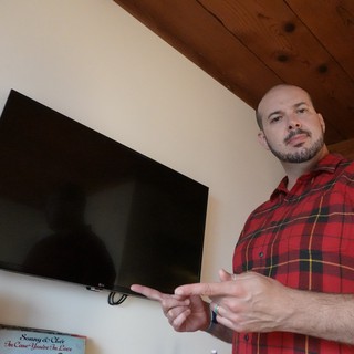Man in Plaid Shirt Gesturing Toward TV