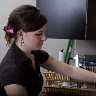 Woman with Orchid Arranges Dishes in Kitchen