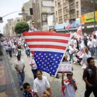 The Great American Walk Caption: Namita Toppo, Tanay Chheda, and a group of 25 people walk down a city street during the 2007 Great American Boycott, carrying an American flag and advocating for immigrant rights.