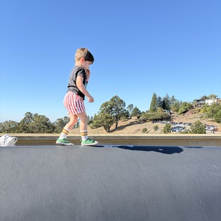 Young Boy Walking on Rooftop Against Clear Blue Sky