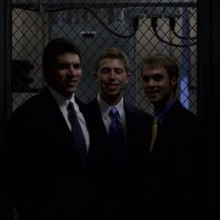 Three Men in Suits Pose in Front of Fence