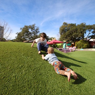 Brothers Playing Superman on Grassy Hill at Park
