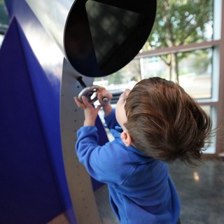 Young Child Exploring Interactive Telescope Exhibit at Science Center