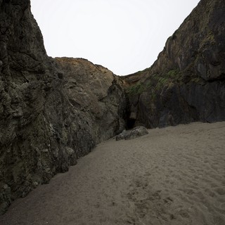 Dark Cave Opening Between Towering Coastal Sea Cliffs