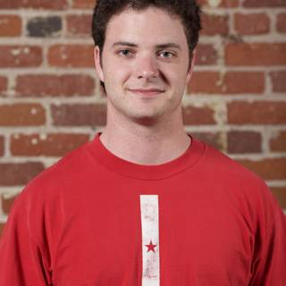 Red Shirted Teenage Boy Smiling in front of Brick Wall