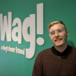 Stylish Man in Glasses Poses in Front of WAG Logo