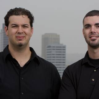 Two Happy Men in Black Shirts Pose in Front of Skyscraper
