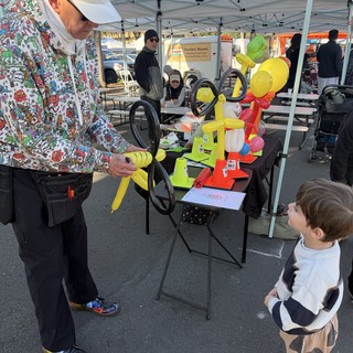 Balloon Artist Delights Young Child at Farmers Market