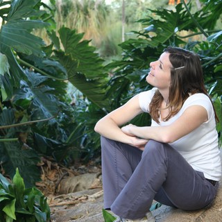 Young Woman Resting Against Palm Tree in Tropical Garden