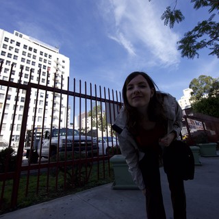Woman Peering Through Iron Fence on City Sidewalk