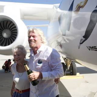 Richard Branson and a Companion Stand Tall Next to an Airplane