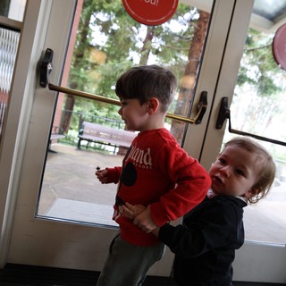 Two Young Children Playing Together at Glass Door Exit