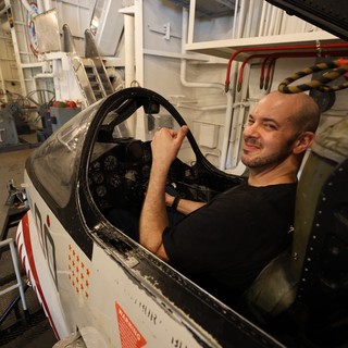 Man Sitting in Vintage Aircraft Cockpit Aboard USS Hornet