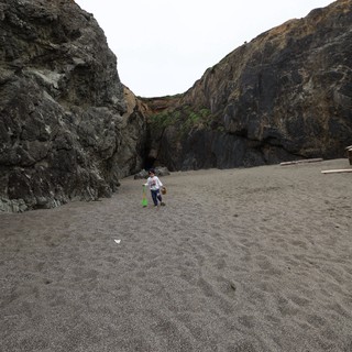 Child Explorer Between Sea Cliffs on Dark Sand Beach