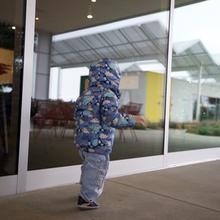 Toddler in Floral Jacket Peering Through Glass Door