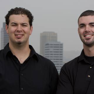 Two Happy Men in Black Shirts Pose in front of Skyscraper