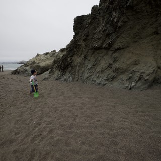 Child Explores Dark Sand Beach Beside Dramatic Cliffs