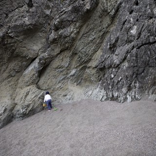 Small Child Explores Towering Sea Cliff at Low Tide