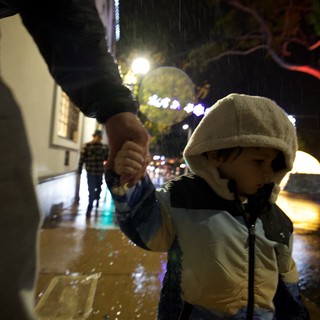Child Walking Through Rain on Illuminated Street at Night