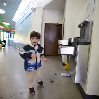 Young Boy Walking Past Water Fountain in School Hallway