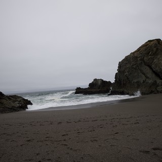 Moody Coastal Cove with Dark Sand and Sea Stacks