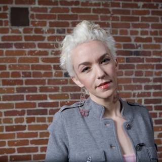White-haired Woman in Gray Jacket Against Brick Wall