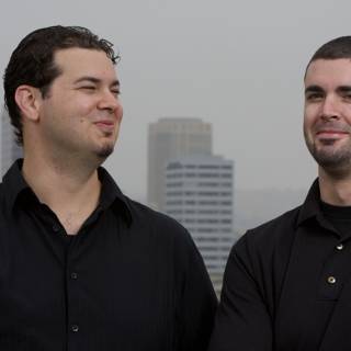Two Happy Men in Black Shirts Pose in Front of Skyscraper