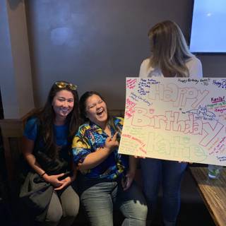 Three Women Celebrate with a Happy Birthday Sign