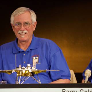 Blue-Shirted Trio Examines Mysterious Gold Object at Phoenix Landing Press Conference