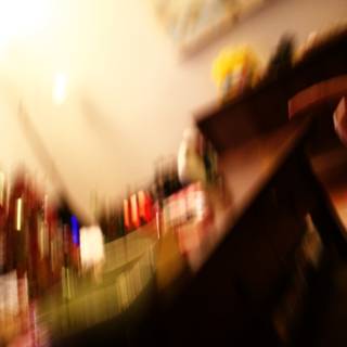 Blurry Finger on Plywood Surface Caption: A person holds a remote control against a background of plywood flooring, shelves, bottle, and furniture in an indoors location in Altadena, California. Tags include recreation, sport, and a pub environment.